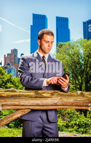 Envoi de SMS à un jeune homme d'affaires. Portant officiellement dans un costume bleu, cravate noire, un jeune homme professionnel est debout devant le quartier des affaires, checki Banque D'Images