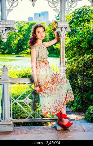 Dame de détente sur le parc. Vêtir de robe longue sans manches, sandales rouges chaussures, une jolie jeune fille est assise sur des rampes à l'intérieur d'un pavillon, attendant f Banque D'Images