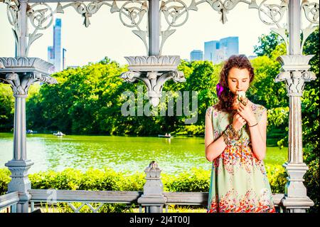 Lady vous a disparu au parc. Jolie jeune fille portant sans manches, longue robe, debout à l'intérieur du pavillon, mains tenant la rose blanche, regardant vers le bas, smelli Banque D'Images