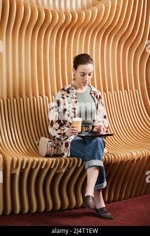 Portrait vertical d'un jeune professionnel utilisant une tablette tout en travaillant dans un espace de bureau moderne avec des chaises de créateur Banque D'Images
