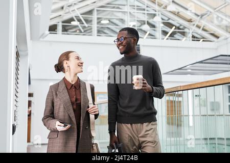 Portrait à la taille de deux jeunes gens d'affaires marchant vers l'appareil photo dans le bâtiment de bureau tout en commençant le travail le matin, espace de copie Banque D'Images