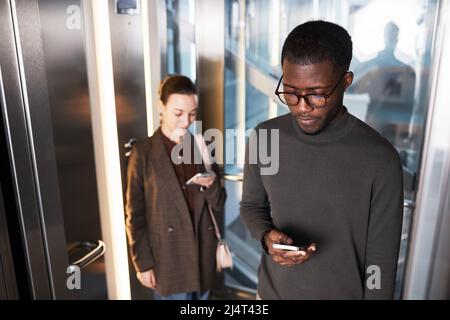 Vue en grand angle de deux jeunes gens d'affaires dans un ascenseur en verre dans un immeuble de bureau moderne, espace de copie Banque D'Images