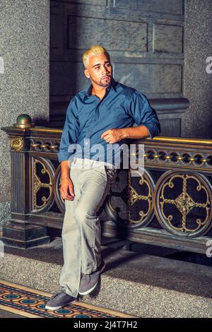 Homme qui vous attend. Porter une chemise bleue, un pantalon gris, des chaussures décontractées, un jeune homme avec la barbe, les cheveux jaunes est debout par la main courante de style ancien dans un Banque D'Images