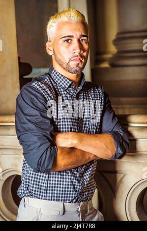 Portrait du jeune travailleur. Porter une chemise noire à motifs, un pantalon gris, croisant les bras, un jeune homme avec la barbe, les cheveux jaunes, est debout par une main courante sur Banque D'Images