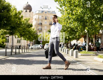 Beau jeune homme d'affaires afro-américain utilisant un téléphone portable tout en traversant une rue Banque D'Images