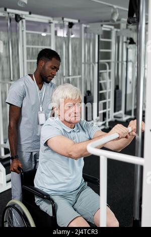 Portrait d'un homme âgé utilisant un fauteuil roulant en salle de gym et effectuant des exercices de réadaptation Banque D'Images