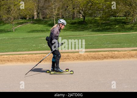 Ski à roulettes ou ski sur terre dans un parc de Londres lors d'une journée de printemps ensoleillée. Femme utilisant des bâtons et des motomarines en ski de fond Banque D'Images