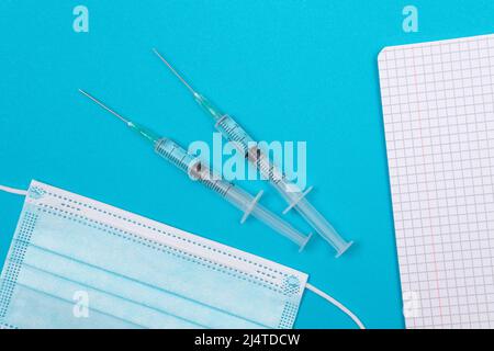 Concept de vaccination, d'immunologie ou de revaccination - deux seringues médicales se trouvant sur une table bleue dans le cabinet du médecin d'un hôpital ou d'une clinique. Ouvert Bloc-notes vide - maquette avec espace de copie Banque D'Images