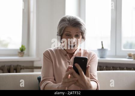 Femme plus âgée regardant à l'écran de téléphone cellulaire avec la bouche ouverte Banque D'Images