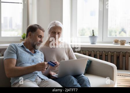 Un couple plus âgé utilise un ordinateur portable et une carte de crédit pour effectuer un achat en ligne Banque D'Images