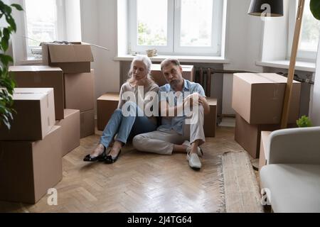 Un couple âgé fatigué s'assoit au sol près des boîtes avec ses effets personnels Banque D'Images