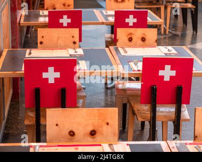 Gruyères, Suisse - 23 novembre 2021 : intérieur d'un restaurant suisse typique à Gruyères avec chaises et drapeau suisse à l'arrière. Banque D'Images