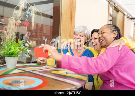 Des amis seniors multiraciaux heureux faisant des appels vidéo avec téléphone mobile au restaurant brunch - concept de technologie de génération de personnes âgées Banque D'Images