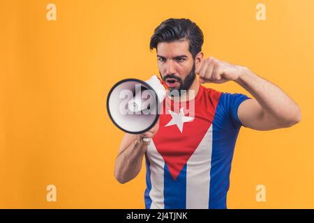 Jeune caucasien barbu dirigeant actif attrayant Happy man 20s portant le drapeau cubain t-shirt parlant dans un haut-parleur isolé sur fond jaune portrait de studio. Photo de haute qualité Banque D'Images