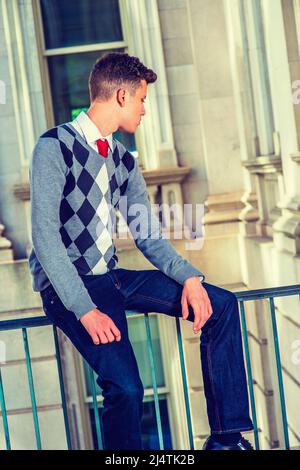 Homme relaxant dehors. Portant un chandail noir, blanc, gris à motifs, un Jean, les mains reposant sur des longueurs, un jeune homme d'affaires charmant est assis sur un R. Banque D'Images