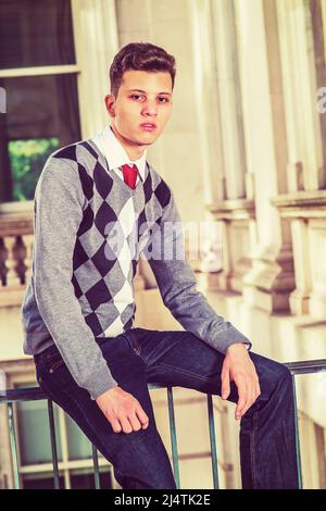 Portrait de l'étudiant de collège. Un jeune homme d'affaires est assis avec un pull à motifs noir, blanc et gris, un Jean, les mains reposant sur des longueurs Banque D'Images