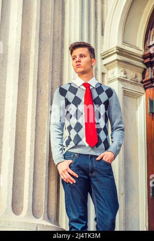 Portrait de l'étudiant de collège. Robe de chambre noire, blanche, grise à motifs, cravate rouge, jeans, un jeune homme d'affaires charmant est debout près d'un pilier Banque D'Images