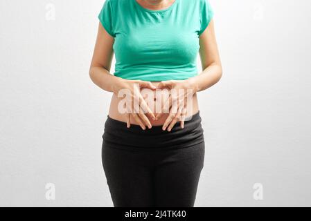 Inreconnaissable femme blanche enceinte paisible qui embrasse son ventre devant un arrière-plan blanc isolé Banque D'Images