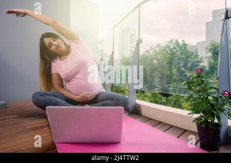 cours de yoga en ligne pour les femmes enceintes pour une vie plus saine, femme sur un tapis rose pratiquant le yoga avec son ordinateur portable à la maison. Banque D'Images