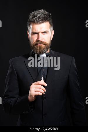 Concept de religion. Beau prêtre hispanique catholique homme sur fond noir isolé. Pasteur ou prédicateur priant, portrait de prêtre de pasteur masculin. Banque D'Images