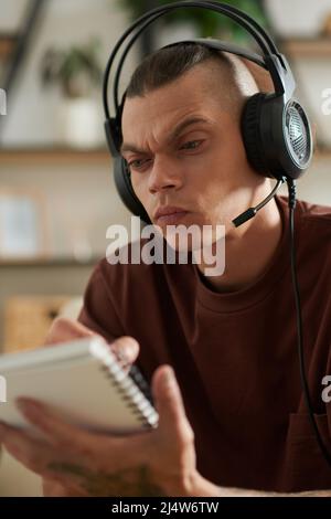 Un jeune homme se frognant à porter un casque lorsque vous regardez une vidéo sur un ordinateur et que vous écrivez des détails Banque D'Images