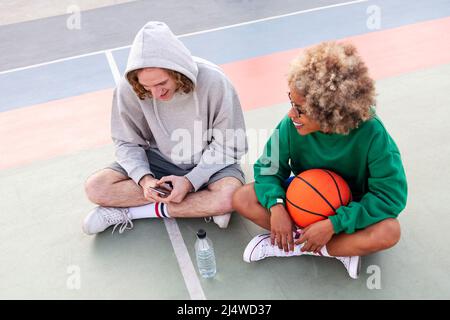 couple d'amis discutant et partageant un bon moment assis sur le terrain après une pratique de basket-ball dans un parc de la ville, concept d'amitié et de sp urbaine Banque D'Images