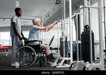 Vue latérale d'un homme en fauteuil roulant utilisant des appareils d'exercice à la clinique de réadaptation, espace de copie Banque D'Images