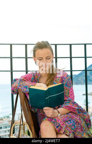 jolie jeune femme assise sur une terrasse au bord de la mer lisant un livre Banque D'Images