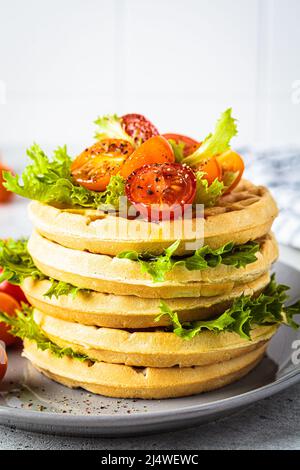 Pile de gaufres savoureuses avec tomates cerises et laitue, gros plan, fond gris, concept petit déjeuner. Banque D'Images