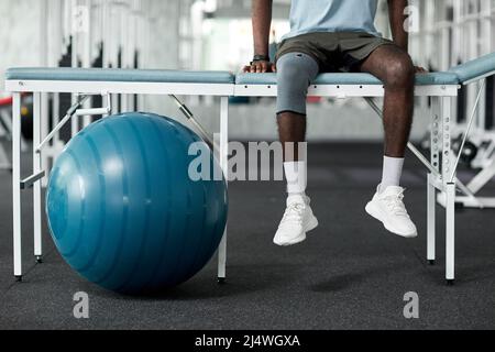 Photo basse section d'un homme afro-américain assis sur un lit de massage dans une clinique de réadaptation Banque D'Images