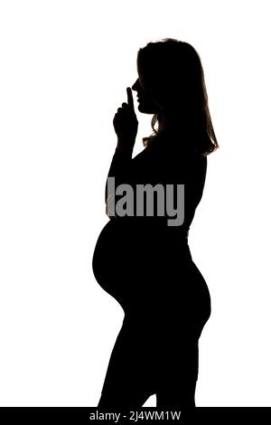 Silhouette d'une femme enceinte avec le doigt sur ses lèvres posé en studio sur un fond blanc Banque D'Images