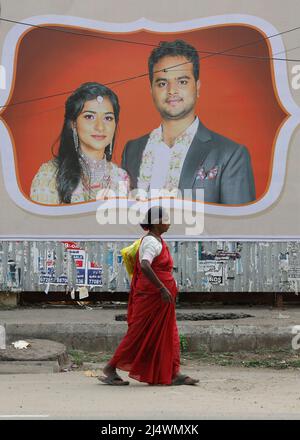 Une vieille femme marchant devant un mur couvert par un poster de campagne électorale à Trichy, Tamil Nadu, Inde Banque D'Images