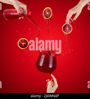 Femme main soutien volent verre de savoureux cocktail avec des oranges de sang et de la glace avec des éclaboussures, des ingrédients tombant à glass. Les mains des femmes versent le jus f Banque D'Images