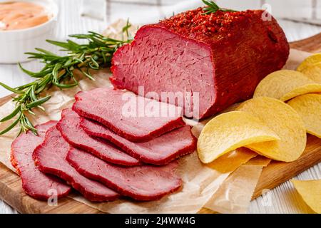 pastrami de bœuf frais tranché sur une planche en bois avec du romarin frais, et des chips de pomme de terre sur une table blanche avec sauce mille îles , vue horizontale de l'abo Banque D'Images