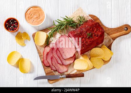 pastrami de bœuf frais tranché sur une planche en bois avec du romarin frais, et des chips de pomme de terre sur une table blanche avec sauce mille îles , vue horizontale de l'abo Banque D'Images