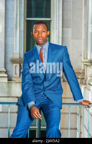 Homme d'affaires qui pense dehors. Dressing formellement en costume bleu, cravate à motifs, un jeune homme noir assis sur une rampe dans un immeuble de bureau de style vintage, moi Banque D'Images