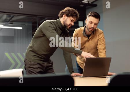 Homme d'affaires concentré pointant vers l'écran d'ordinateur portable, travaillant sur un projet d'entreprise avec un collègue de sexe masculin dans un bureau moderne Banque D'Images