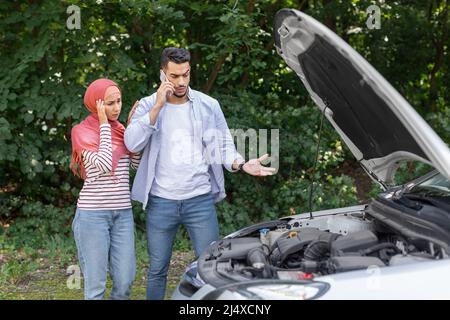 Triste femme arabe déjumelée dans le hijab et homme appel à l'auto-assistance, se tenir près de la voiture cassée avec le capot ouvert Banque D'Images