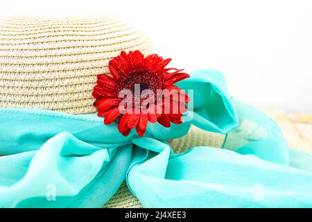 Fleur de gerbera rouge sur un chapeau de paille attaché avec un foulard bleu, été , plage, fond romantique Banque D'Images