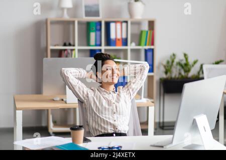 Une employée de bureau heureuse s'est penchée sur une chaise, se relaxant après avoir travaillé avec succès sur son lieu de travail au bureau Banque D'Images