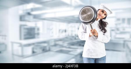 Cuisinez une fille brunette souriant avec une poêle derrière dans une cuisine. Banque D'Images