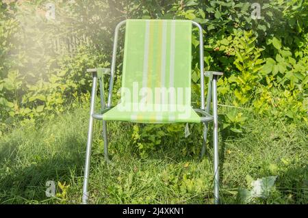 Une chaise de jardin pliante vide pour se détendre se tient sur l'herbe verte sur la pelouse lors d'une journée d'été ensoleillé, une copie de l'espace. Banque D'Images