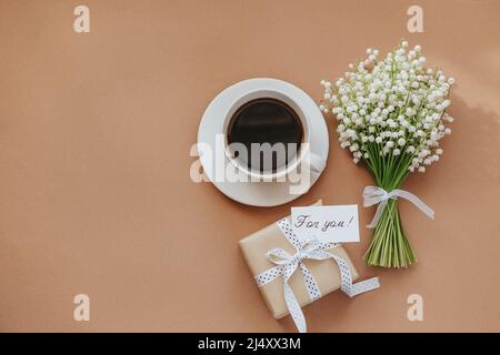 Bouquet de fleurs de Lily de la vallée, cadeau et tasse de café sur fond beige. Banque D'Images