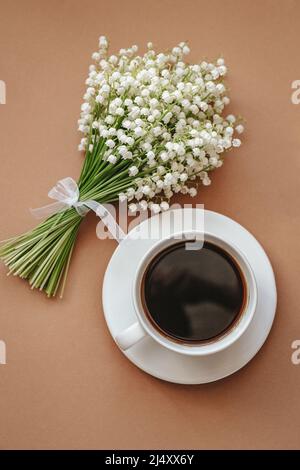 Tasse à café avec bouquet de fleurs lis de la vallée sur fond beige vue de dessus. Pose à plat. Banque D'Images