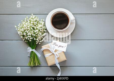 Bouquet de fleurs de Lily de la vallée, cadeau et tasse de café sur fond de bois gris. Banque D'Images