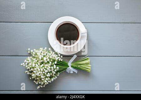 Bouquet de fleurs de Lily de la vallée et tasse de café sur fond de bois gris. Banque D'Images