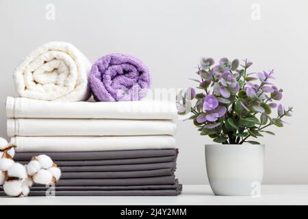 Pile de linge de lit, draps et serviettes avec branche de coton et plante en pot sur la table Banque D'Images