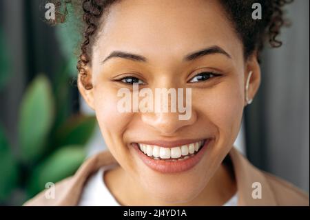 Gros plan photo d'une belle jeune femme afro-américaine aux cheveux bouclés positifs, fille de race mixte avec des taches de rousseur, regardant l'appareil photo, souriant, montrant son sourire blanc de neige Banque D'Images