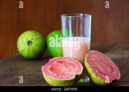Verre avec jus de goyave demi-fruits à côté du verre et fruits entiers dans un fond flou Banque D'Images