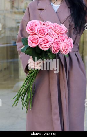 Femme élégante en long beige manteau holdind beau bouquet mono de roses roses. Banque D'Images